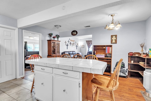 2004 N Monticello St, Big Spring, TX 79720 - kitchen with tile countertops, a breakfast bar area, white cabinets, pendant lighting, and light tile patterned floors