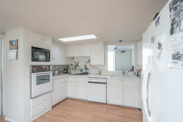 kitchen featuring light countertops, light wood-style floors, white cabinets, a sink, and white appliances