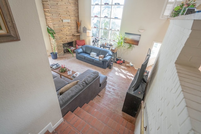 living room with brick floor, baseboards, a stone fireplace, and a towering ceiling