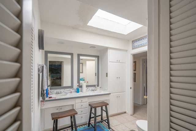 bathroom with double vanity, a skylight, a sink, and tile patterned floors