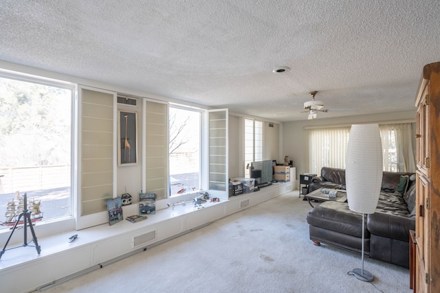 living room featuring ceiling fan, visible vents, a textured ceiling, and light colored carpet