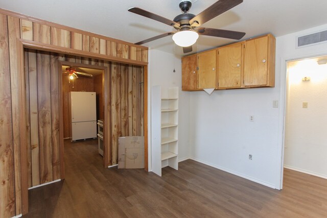 interior space featuring wooden walls, dark hardwood / wood-style floors, white fridge, and ceiling fan