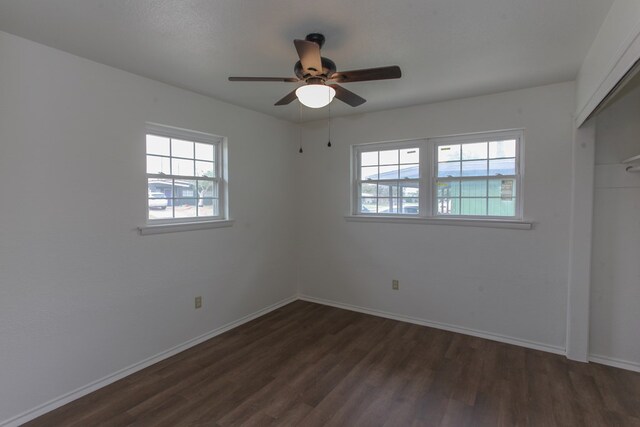 unfurnished bedroom with multiple windows, ceiling fan, a closet, and dark wood-type flooring