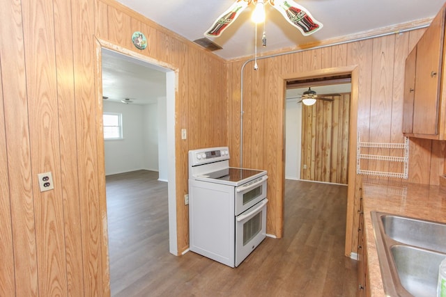 kitchen featuring ceiling fan, wooden walls, sink, wood-type flooring, and white electric stove