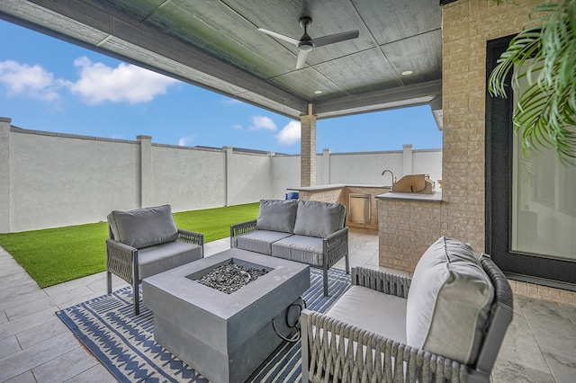 view of patio / terrace with exterior kitchen, an outdoor living space with a fire pit, a fenced backyard, and a ceiling fan