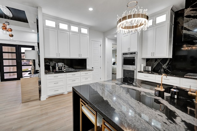 kitchen featuring double oven, light wood-type flooring, white cabinetry, and dark stone countertops