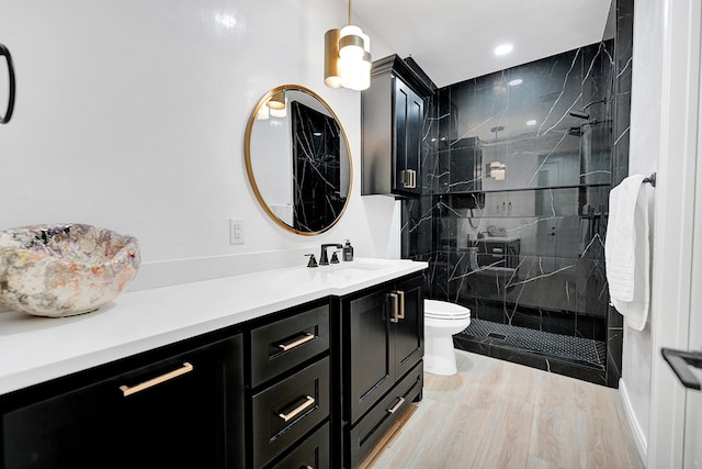 bathroom with toilet, vanity, a marble finish shower, and wood finished floors