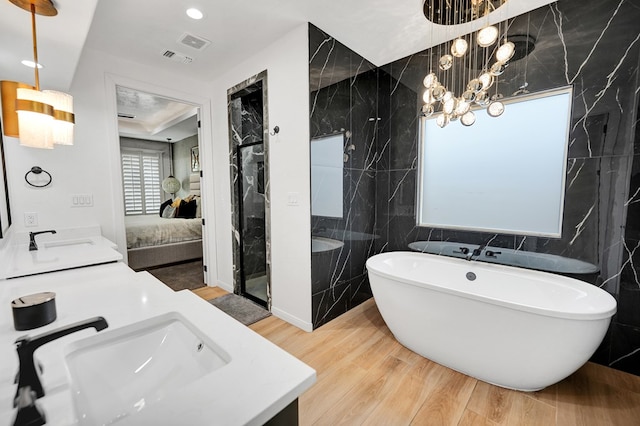 ensuite bathroom featuring tile walls, visible vents, a soaking tub, wood finished floors, and a sink