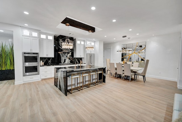 kitchen with light wood-style floors, appliances with stainless steel finishes, a large island, backsplash, and a kitchen bar