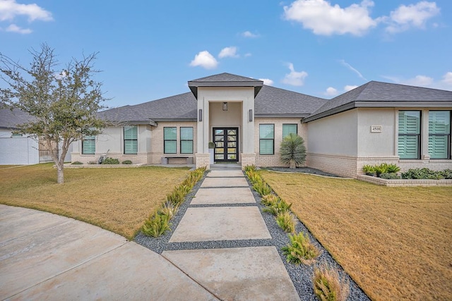 prairie-style house with french doors, brick siding, a front yard, and stucco siding