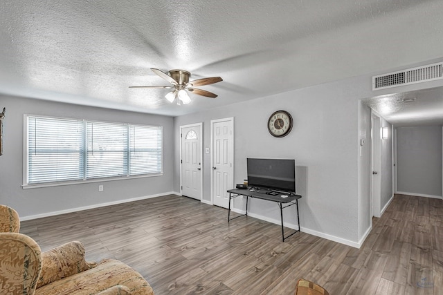living area featuring visible vents, a ceiling fan, a textured ceiling, and wood finished floors