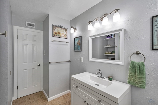 bathroom with a textured ceiling, visible vents, vanity, baseboards, and tile patterned floors