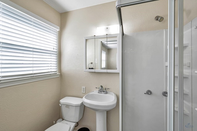 bathroom with an enclosed shower, a textured wall, toilet, and a sink