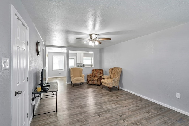 sitting room with a textured wall, wood finished floors, baseboards, a textured ceiling, and a ceiling fan