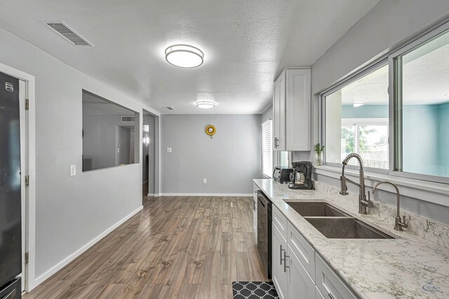 kitchen featuring a sink, dishwasher, white cabinetry, wood finished floors, and visible vents