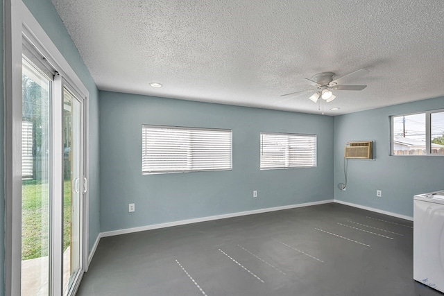 unfurnished room featuring ceiling fan, an AC wall unit, a textured ceiling, baseboards, and washer / dryer