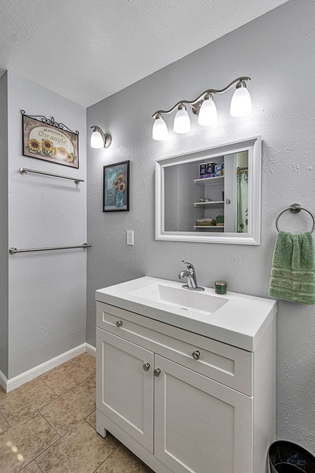 bathroom featuring tile patterned flooring, a textured ceiling, baseboards, and vanity