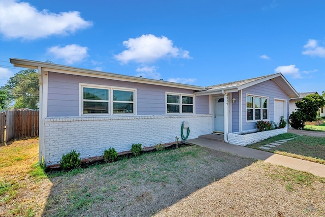 single story home featuring brick siding, an attached garage, fence, and a front yard
