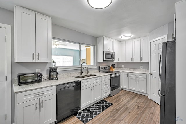 kitchen with a sink, light stone counters, black appliances, light wood-style floors, and white cabinetry