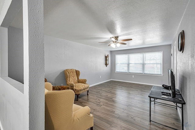 living area with baseboards, a textured ceiling, ceiling fan, and wood finished floors