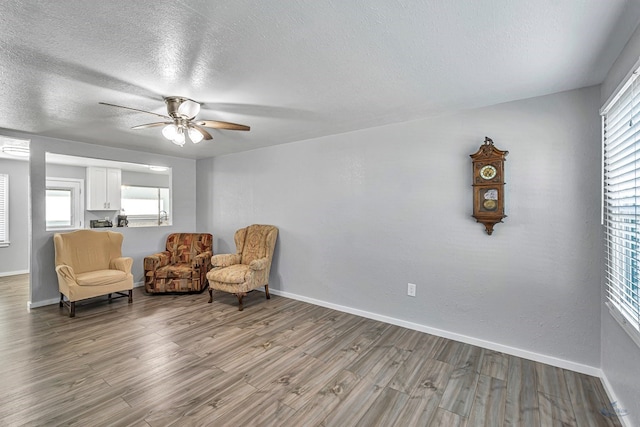 living area featuring a ceiling fan, baseboards, wood finished floors, and a textured ceiling