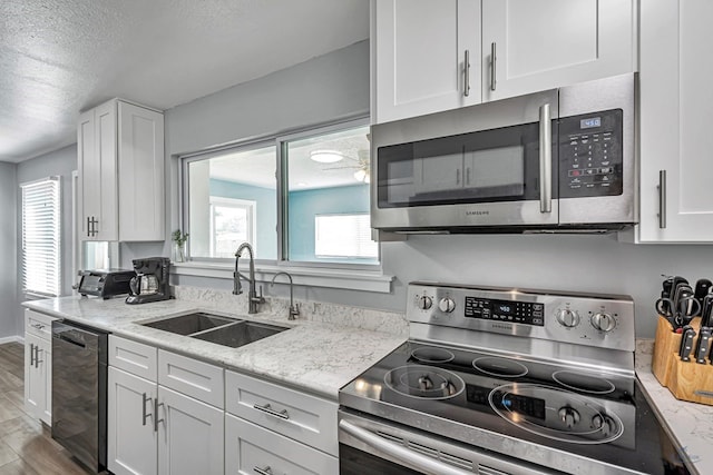 kitchen featuring a textured ceiling, wood finished floors, a sink, white cabinets, and stainless steel appliances