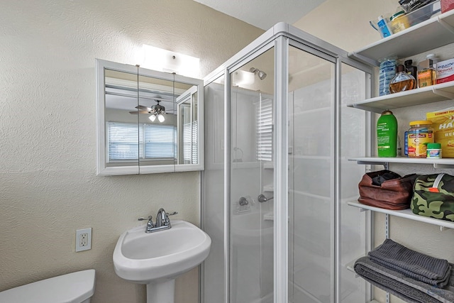 full bath featuring ceiling fan, a stall shower, a sink, toilet, and a textured wall