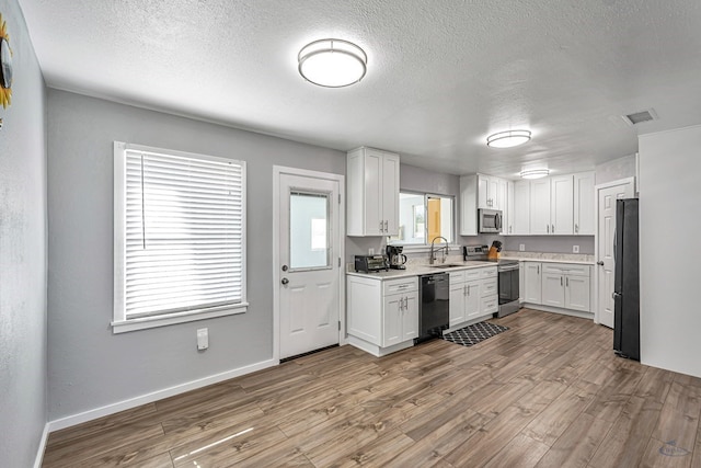 kitchen featuring visible vents, wood finished floors, white cabinetry, a sink, and black appliances