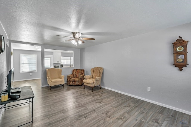 sitting room featuring baseboards, a textured ceiling, ceiling fan, and wood finished floors