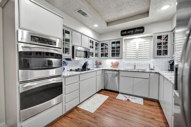 4107 Crestgate Ave, Midland, TX 79707 - kitchen featuring stainless steel appliances, a textured ceiling, a sink, backsplash, and light wood-style floors