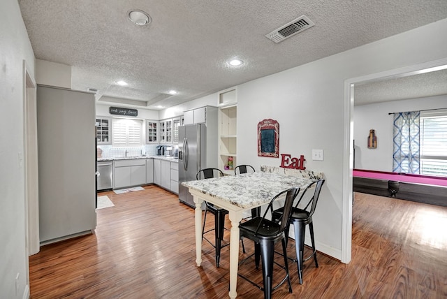 4107 Crestgate Ave, Midland, TX 79707 - kitchen featuring appliances with stainless steel finishes, a peninsula, a textured ceiling, wood finished floors, and glass insert cabinets