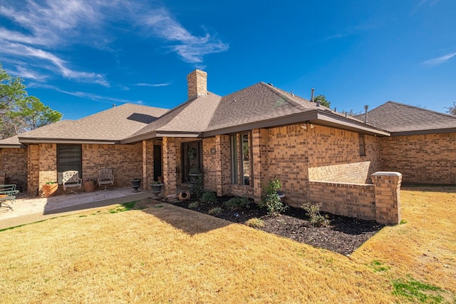 view of front of house with brick siding, a shingled roof, a front yard, a chimney, and a patio area