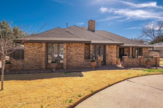 exterior space with brick siding, a front yard, a chimney, and a shingled roof