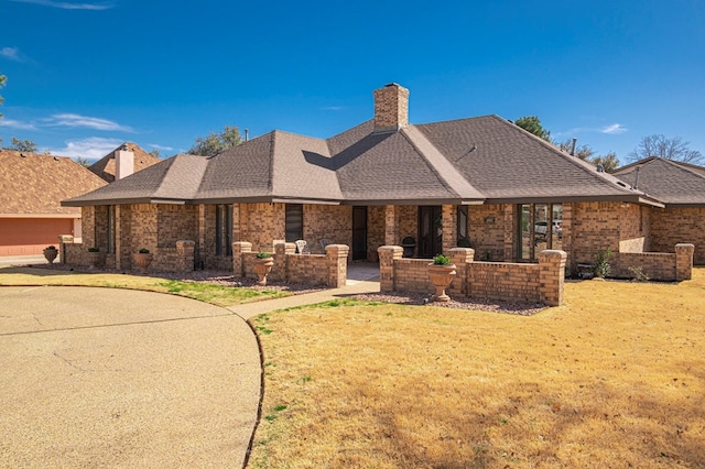 view of front of home with a shingled roof, a chimney, a front lawn, and brick siding