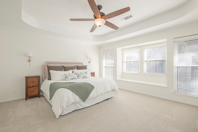 carpeted bedroom featuring a ceiling fan, visible vents, baseboards, ornamental molding, and a raised ceiling