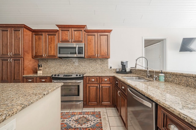 kitchen with stainless steel appliances, a sink, light stone counters, and decorative backsplash