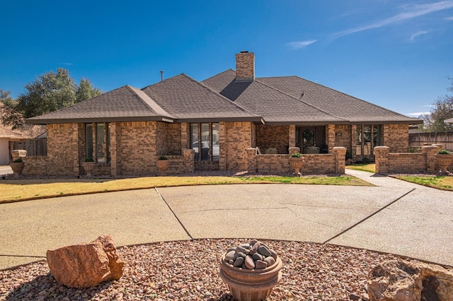 view of front of property featuring brick siding, a chimney, a shingled roof, and fence