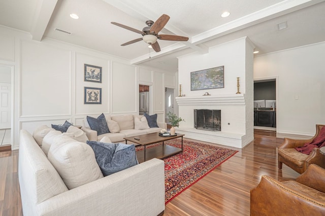 living area with visible vents, a decorative wall, beam ceiling, and wood finished floors