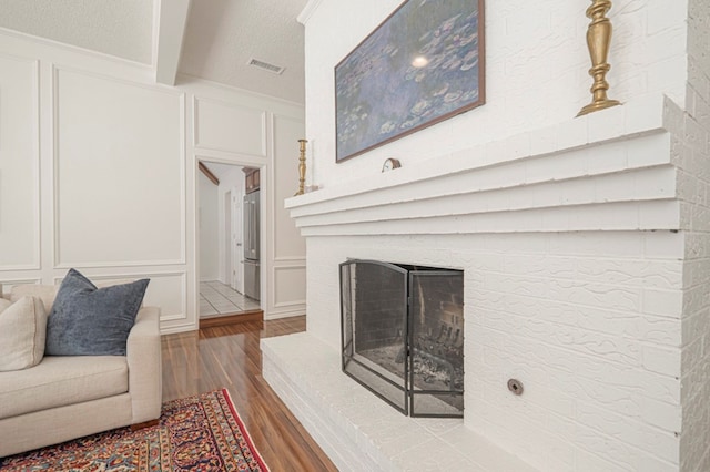 living area featuring a brick fireplace, visible vents, a decorative wall, and wood finished floors