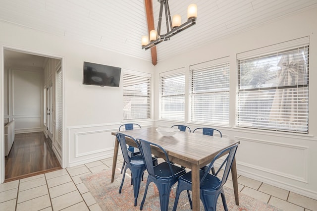 dining area featuring lofted ceiling, light tile patterned floors, a wainscoted wall, and an inviting chandelier