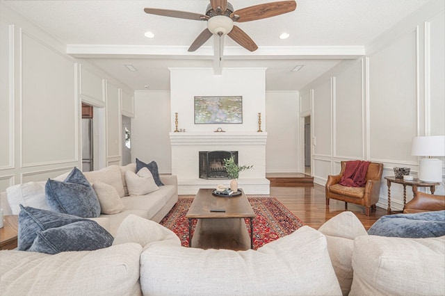 living area featuring a fireplace with raised hearth, recessed lighting, a decorative wall, wood finished floors, and a ceiling fan