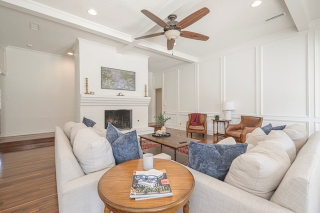 living area with visible vents, a decorative wall, a fireplace with raised hearth, and wood finished floors