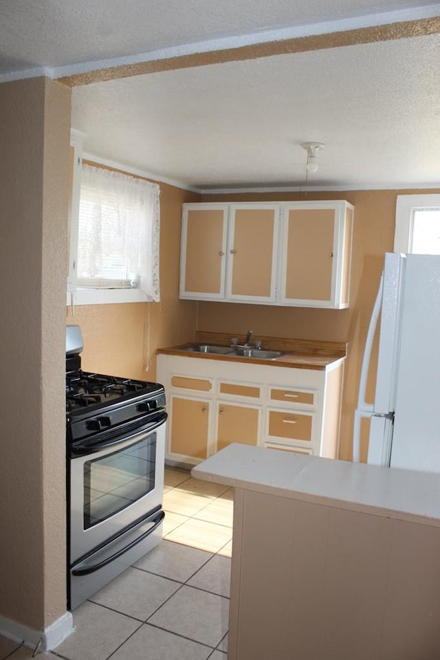 kitchen with sink, light tile patterned floors, white fridge, white cabinetry, and range with gas cooktop