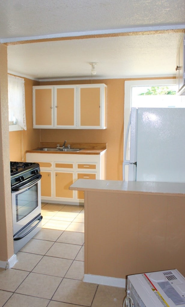 kitchen featuring white refrigerator, light tile patterned floors, sink, and range with gas cooktop