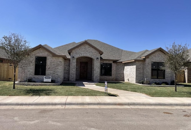 french provincial home featuring brick siding, roof with shingles, and a front lawn