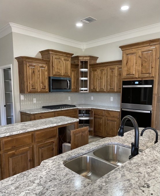 kitchen with brown cabinetry, backsplash, dobule oven black, and a sink