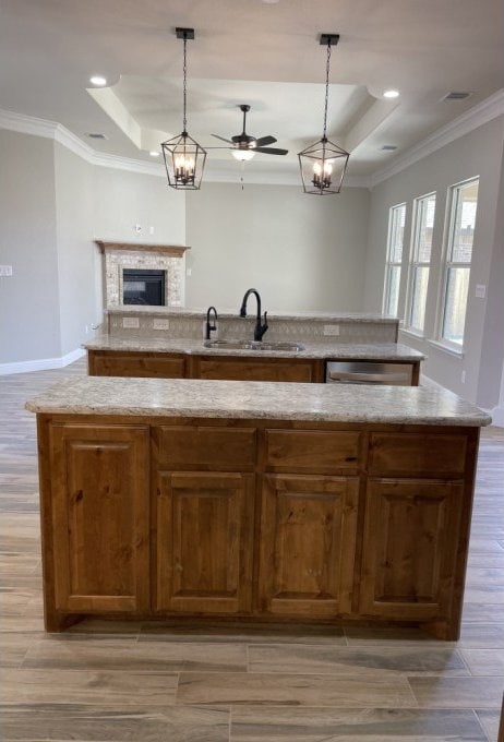 kitchen featuring open floor plan, a center island with sink, ornamental molding, a raised ceiling, and a sink