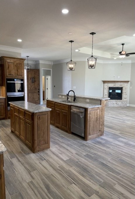 kitchen with a center island with sink, a sink, a glass covered fireplace, light wood-style floors, and appliances with stainless steel finishes