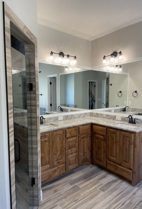 bathroom with a sink, a stall shower, wood finished floors, and double vanity