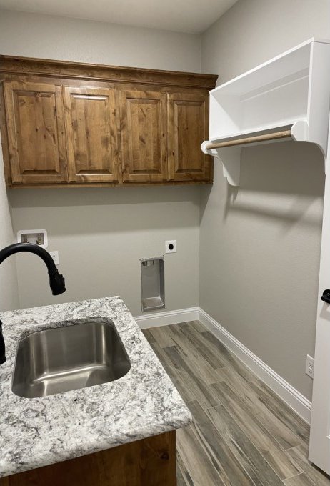 interior space featuring light stone counters, brown cabinetry, wood finished floors, baseboards, and a sink